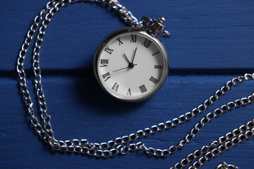 Silver pocket clock with chain on blue wooden table, top view