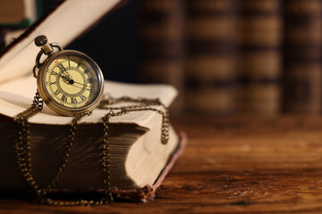 Pocket clock with chain and book on wooden table, closeup. Space for text