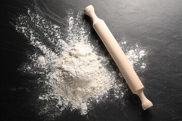 Pile of flour and rolling pin on black textured table, top view