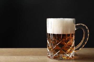 Mug with fresh beer on wooden table against black background. Space for text