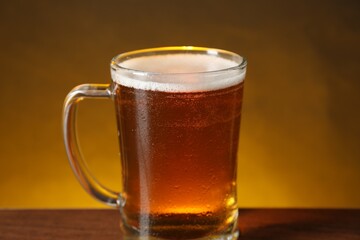 Mug with fresh beer on wooden table against dark background, closeup