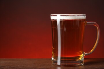 Mug with fresh beer on wooden table against color background, closeup. Space for text