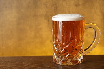Mug with fresh beer on wooden table against yellow background, closeup. Space for text