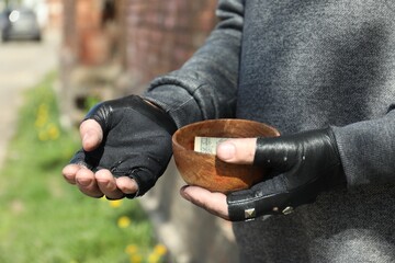 Poor homeless man holding bowl with donations outdoors, closeup