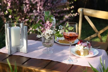 Vase with spring flowers, wine and cake on table served for romantic date in garden