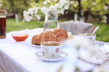 Stylish table setting with tea and croissants in spring garden