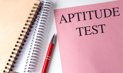 APTITUDE TEST text on pink paper with notebooks