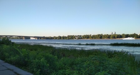 Embankment of the Dnipro River, plants on the shore and yacht, metro bridge
