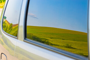 reflection of a beautiful picturesque field in the side window of a car. concept of traveling by...