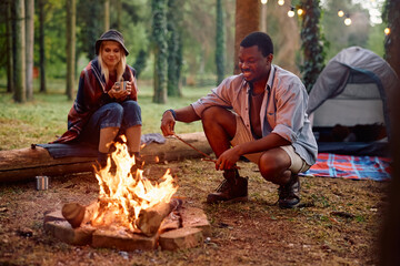 Happy couple of campers enjoying by bonfire in forest.