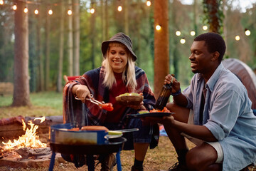 Happy couple of campers preparing food on barbecue grill in nature.