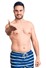 Fototapeta premium Young handsome man wearing swimwear smiling cheerful offering palm hand giving assistance and acceptance.