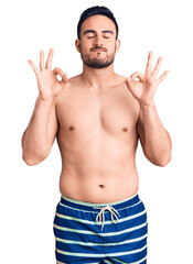 Fototapeta premium Young handsome man wearing swimwear relaxed and smiling with eyes closed doing meditation gesture with fingers. yoga concept.