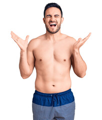 Fototapeta premium Young handsome man wearing swimwear celebrating mad and crazy for success with arms raised and closed eyes screaming excited. winner concept
