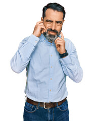 Middle aged man with beard wearing business shirt covering ears with fingers with annoyed expression for the noise of loud music. deaf concept.