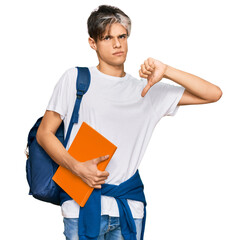 Young hispanic man wearing student backpack and holding books with angry face, negative sign showing dislike with thumbs down, rejection concept