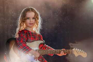 little girl holds a guitar and sits against the curtain in the rays of the spotlights.