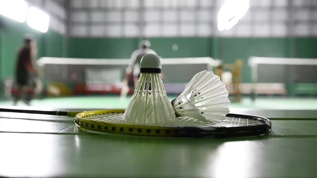 Badminton rackets and white cream badminton shuttlecocks after playing or after games on green floor in indoor badminton court soft focus concept for badminton lovers around the world.