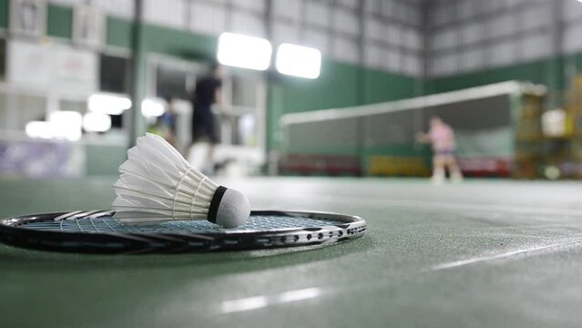 Badminton rackets and white cream badminton shuttlecocks after playing or after games on green floor in indoor badminton court soft focus concept for badminton lovers around the world.