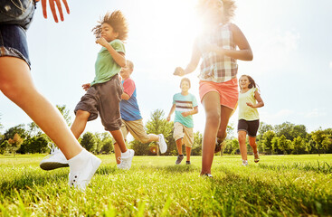 Happy children, playing and running with grass field in nature for fun, playful day or sunshine at park. Diversity or group of excited kids or youth enjoying sunny outdoor holiday or weekend together