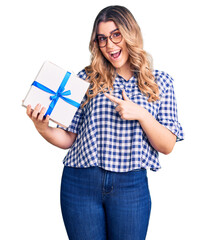 Young caucasian woman holding gift smiling happy pointing with hand and finger