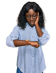 Beautiful african young woman wearing casual clothes and glasses looking at the watch time worried, afraid of getting late