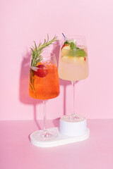 Two colourful cocktails with ice on podiums on pink background.