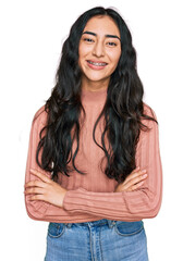 Hispanic teenager girl with dental braces wearing casual clothes happy face smiling with crossed...