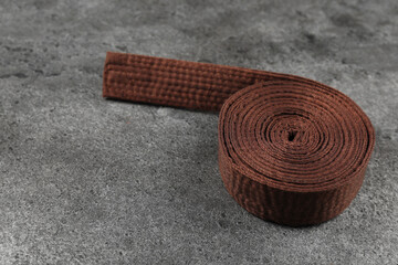 Brown karate belt on gray textured background, space for text