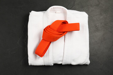 Orange karate belt and white kimono on gray background, top view