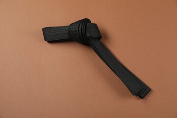 Black karate belt on brown background, top view. Space for text