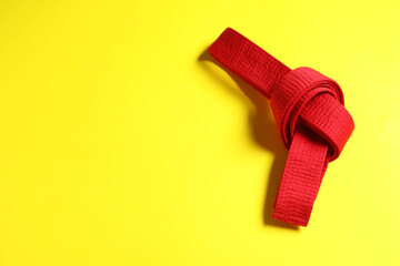 Red karate belt on yellow background, top view. Space for text