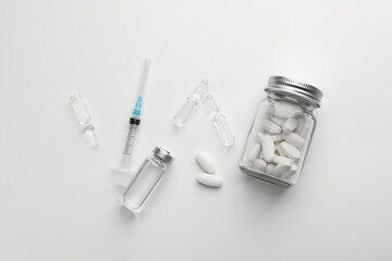 Glass ampoules with liquid, pills and syringe on white background, flat lay