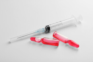 Glass ampoules with liquid and syringe on white background