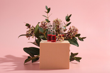 Stylish presentation of skincare ampoules and flowers on pink background
