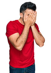 Hispanic man with beard wearing casual red t shirt with sad expression covering face with hands while crying. depression concept.