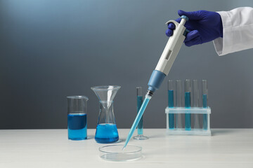 Laboratory analysis. Scientist dripping sample with micropipette into petri dish at white wooden table, closeup