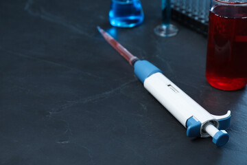 Laboratory analysis. Micropipette with liquid on black table, closeup. Space for text