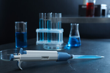Laboratory analysis. Micropipette with liquid and different glassware on black table