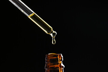 Dripping tincture from pipette into bottle on black background, closeup