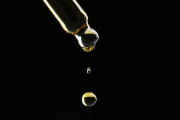 Dripping tincture from pipette on black background, closeup