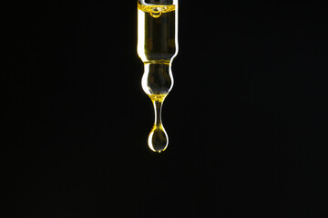 Dripping tincture from pipette on black background, closeup