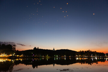 Wat Doi Saket stupa view from the lake at night during Yee Peng festival. Sky lanterns at night.