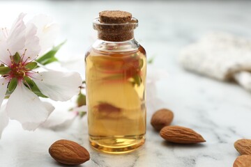 Almond oil in bottle, flower and nuts on white marble table, closeup