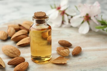 Almond oil in bottle and nuts on color marble table, closeup. Space for text