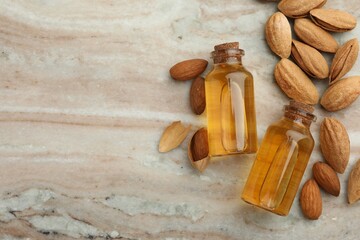 Almond oil in bottles and nuts on color marble table, flat lay. Space for text