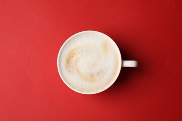 Tasty cappuccino in coffee cup on red background, top view