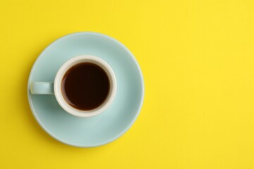 Tasty coffee in cup on yellow background, top view. Space for text