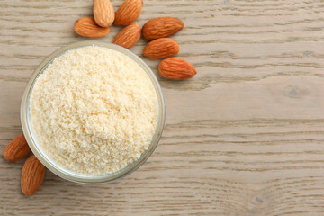 Fresh almond flour in bowl and nuts on wooden table, top view. Space for text