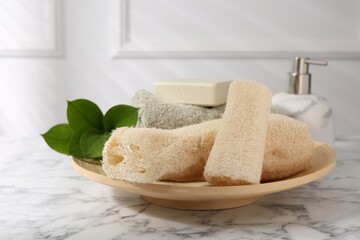 Loofah sponges, soap, towel and green leaves on white marble table